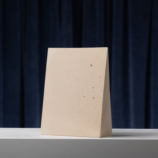 Beige wedge-shaped object on a white surface with a dark blue curtain background