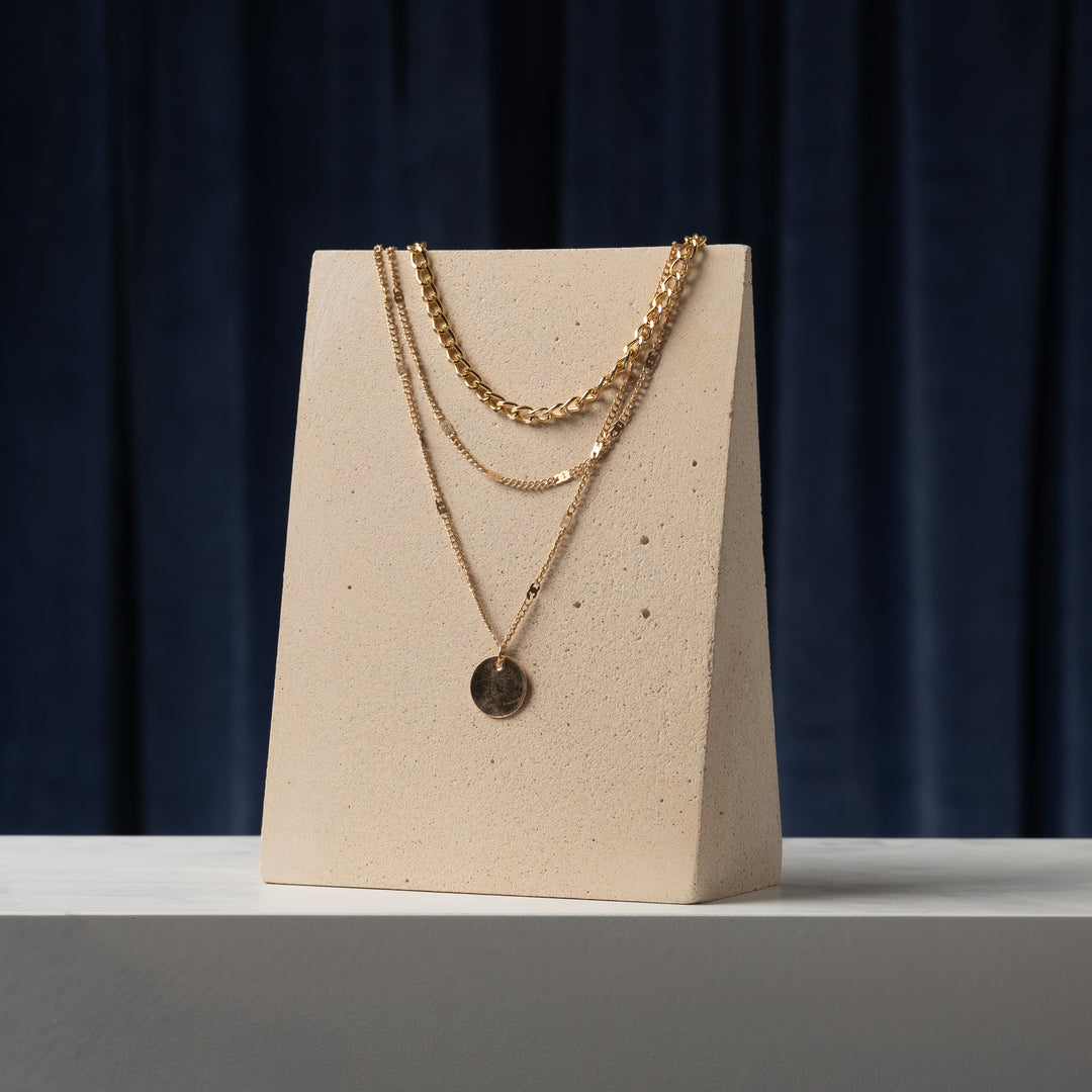 Slanted necklace display block in beige mineral plaster with layered gold necklaces for boutique jewelry retail display