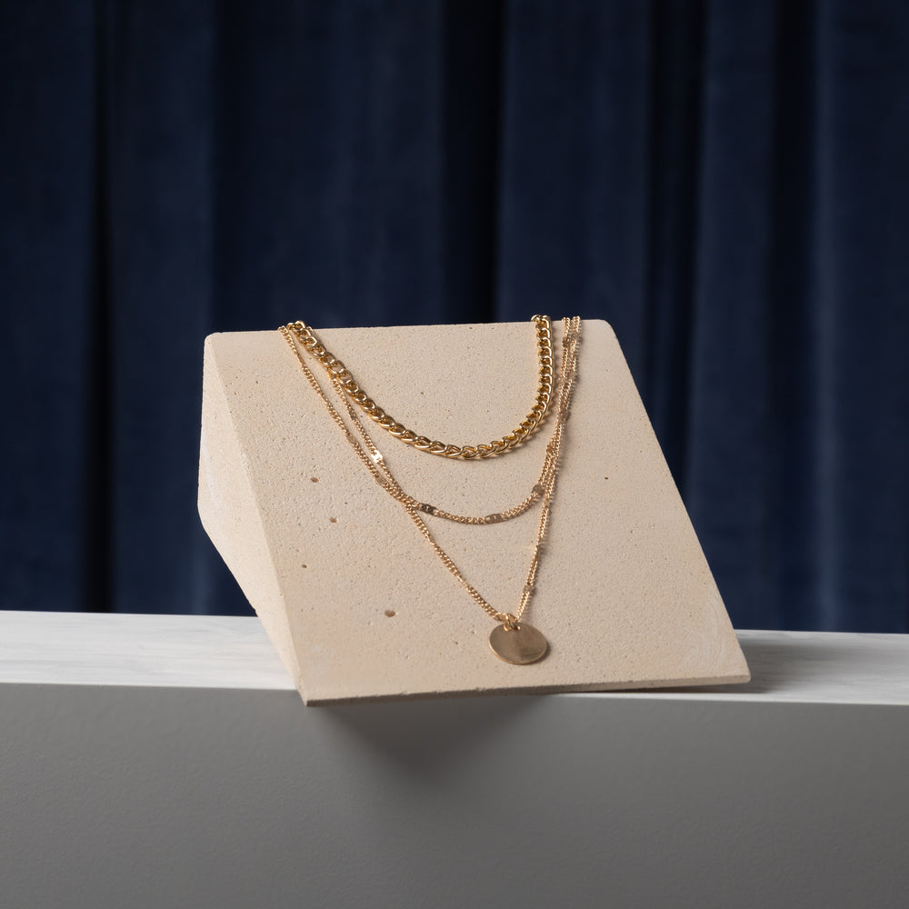 Minimal slanted necklace display block in matte mineral plaster for jewelry showroom and retail presentation