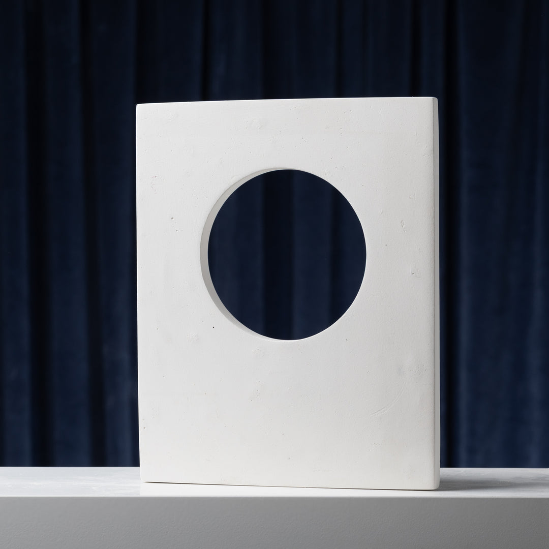 Sculptural cut-out styling panel in white mineral plaster with circular opening for product photography and editorial styling