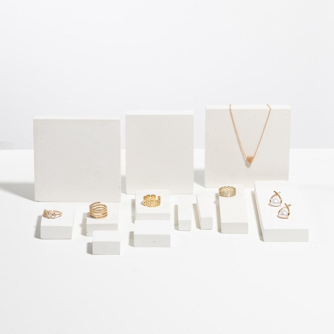 Gold rings, pearl earrings and pendant necklace displayed on white modular jewelry display blocks