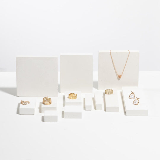 Gold rings, pearl earrings and pendant necklace displayed on white modular jewelry display blocks