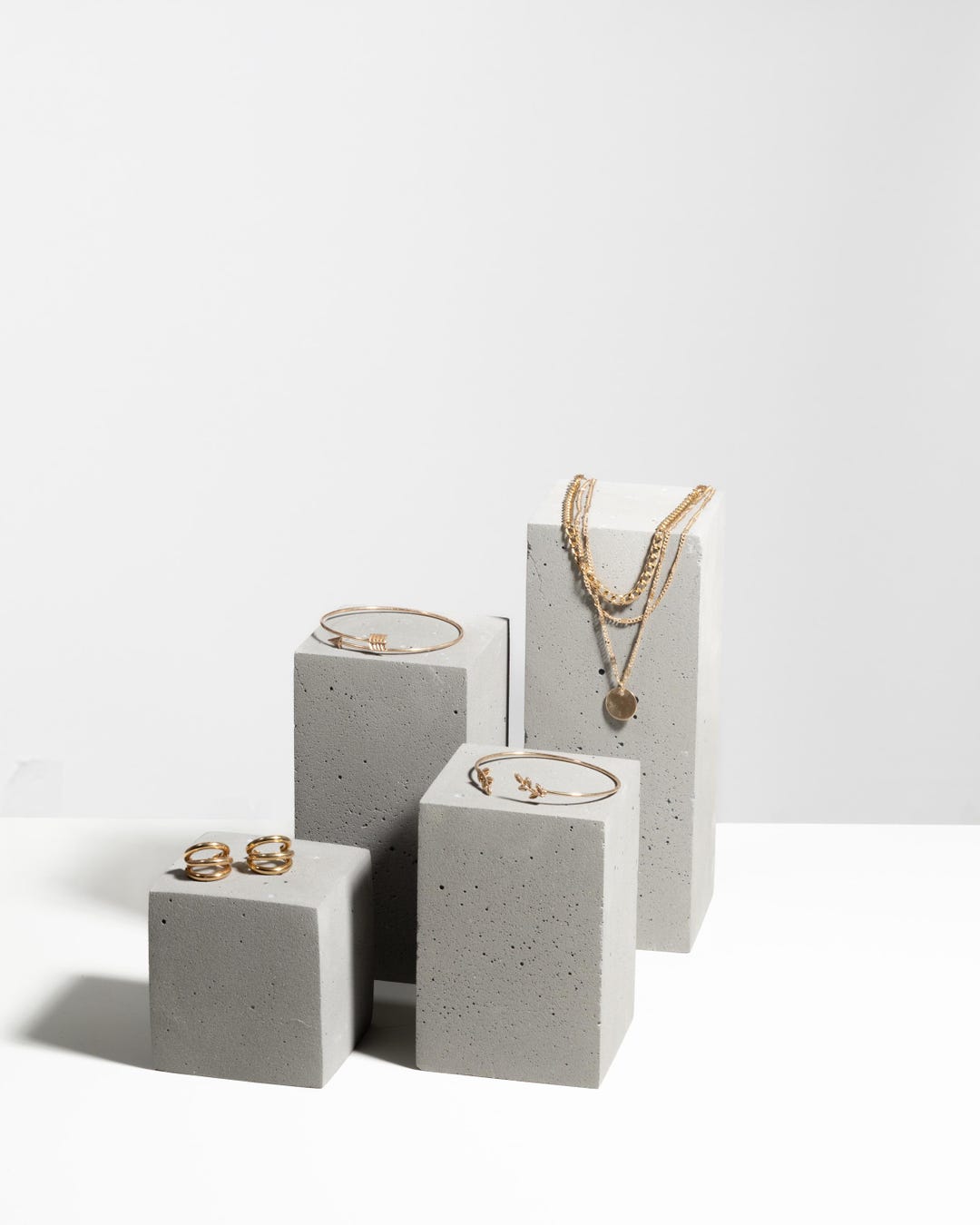Gold rings, bracelets and layered necklace displayed on grey concrete pedestal blocks