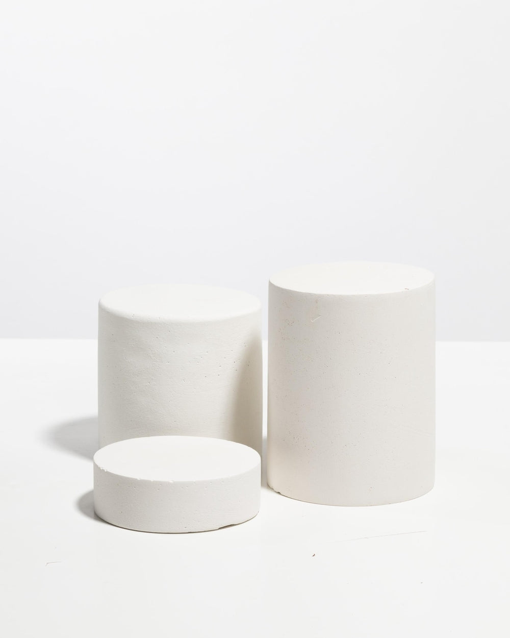 Set of three matte white cylinder display pedestals in varying heights