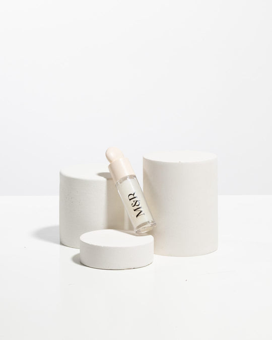 Cosmetic dropper bottle styled between matte white cylinder display pedestals
