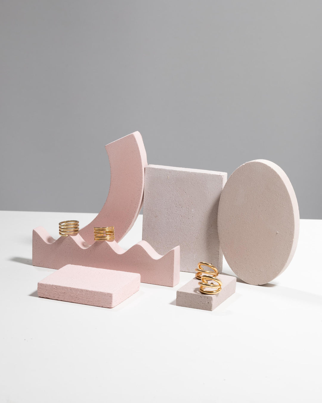 Gold rings displayed on pink wavy ring holder and rectangular block