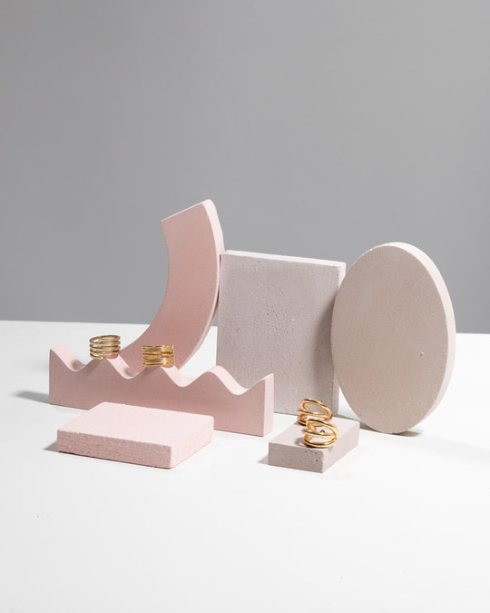 Gold rings displayed on pink wavy ring holder and rectangular block