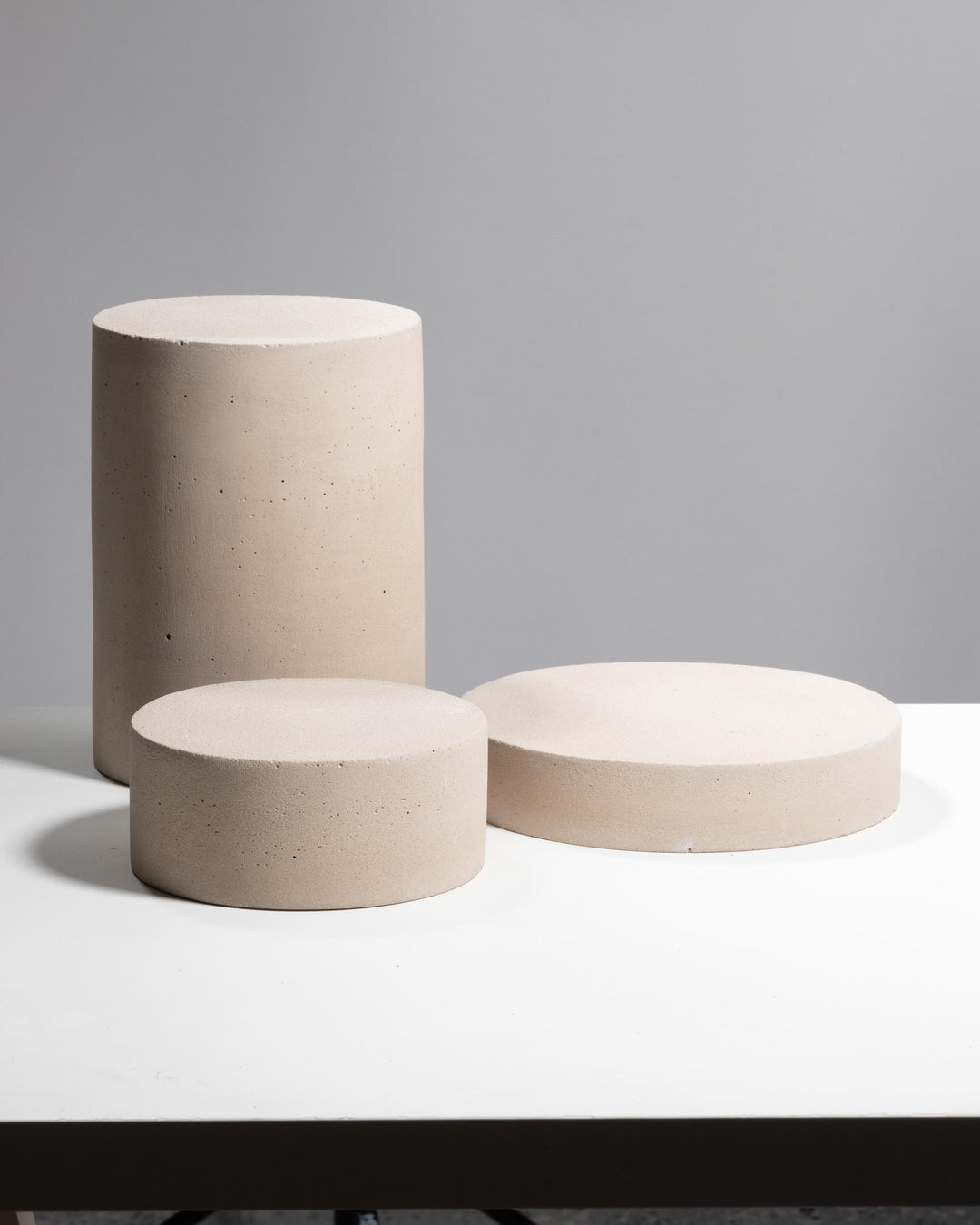 Three cylindrical display pedestals in light beige concrete with matte finish