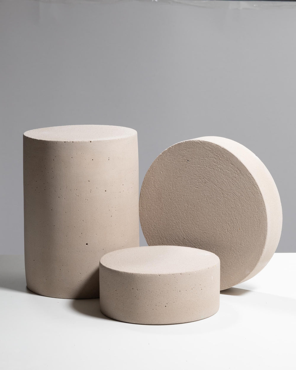 Three warm gray cylindrical concrete display pedestals of varying heights