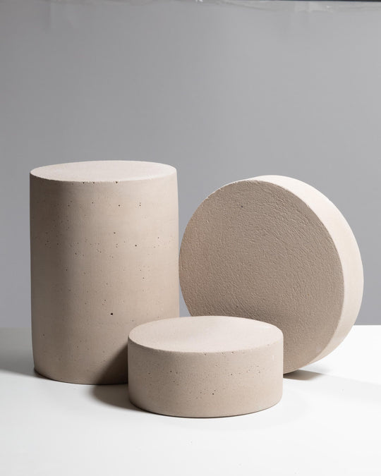 Three warm gray cylindrical concrete display pedestals of varying heights