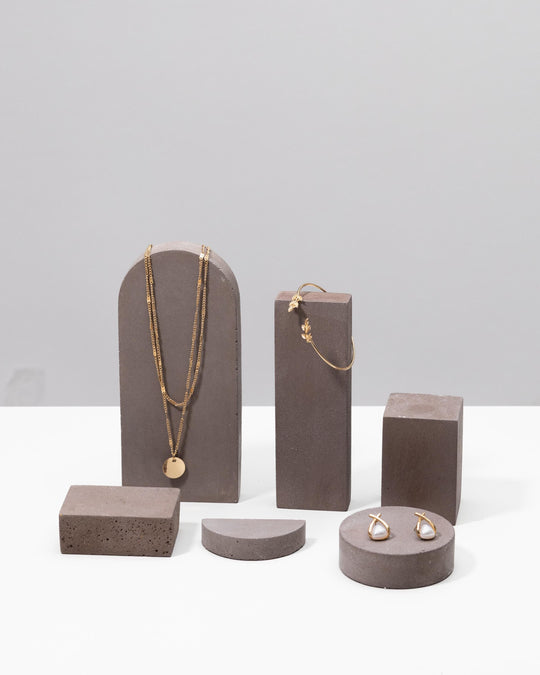 Gold jewelry displayed on grey plaster geometric display pedestals