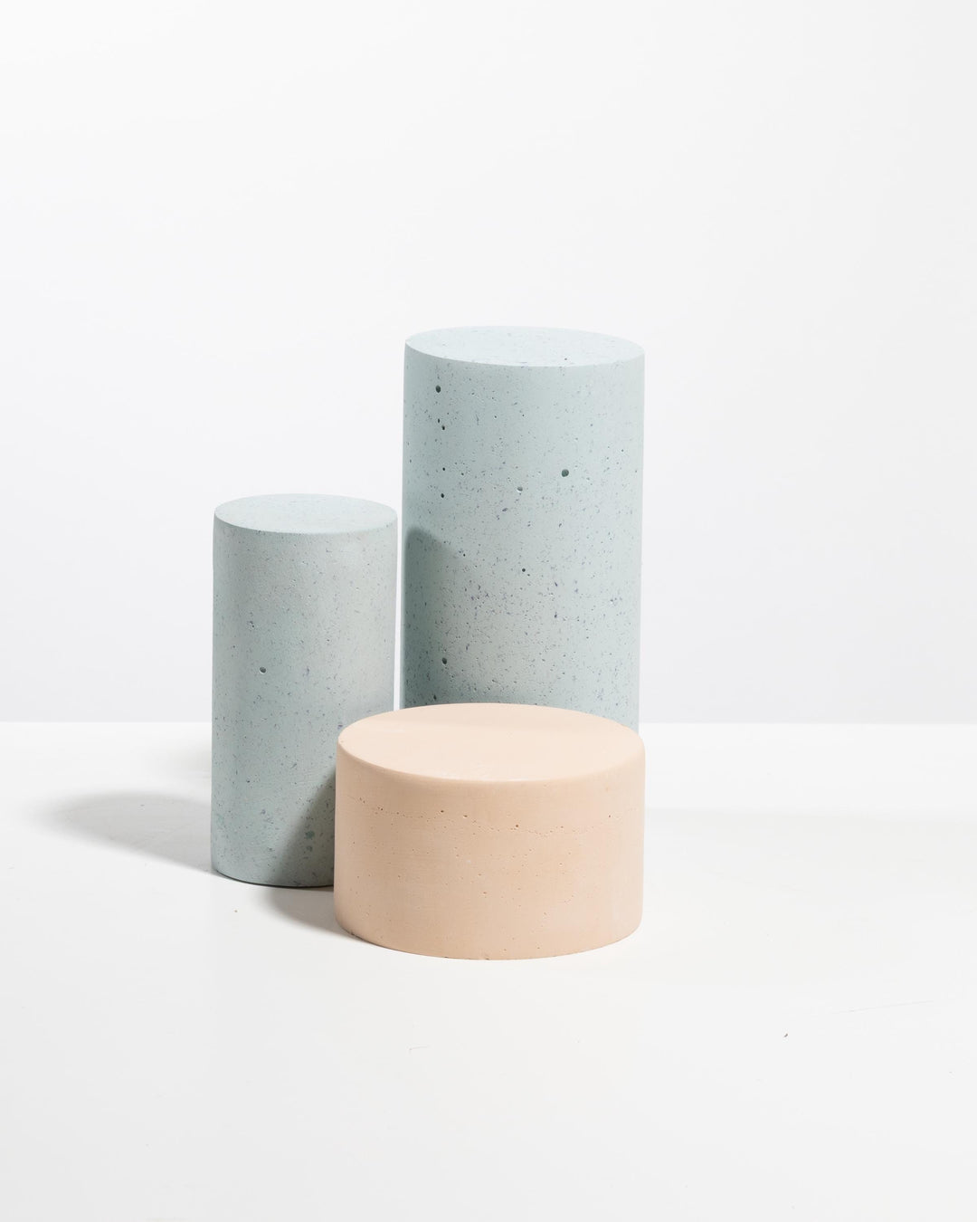 Three cylinder display podiums: two light blue speckled pedestals and one pale peach pedestal