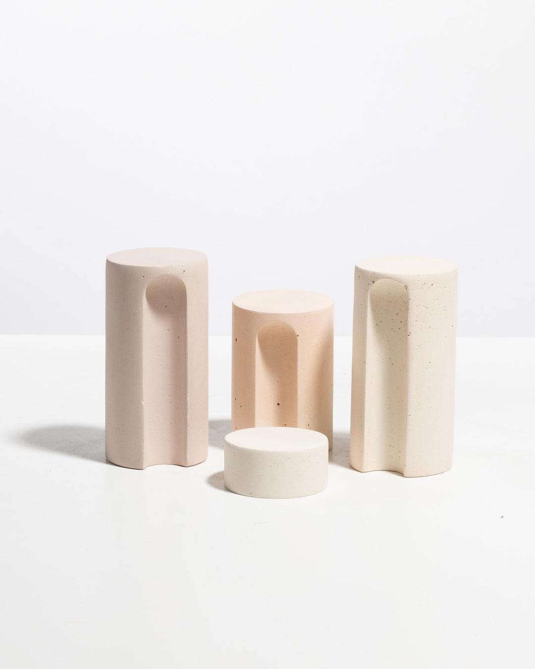 Four pale pink and cream cylinder pedestals with arched cutouts in graduated heights
