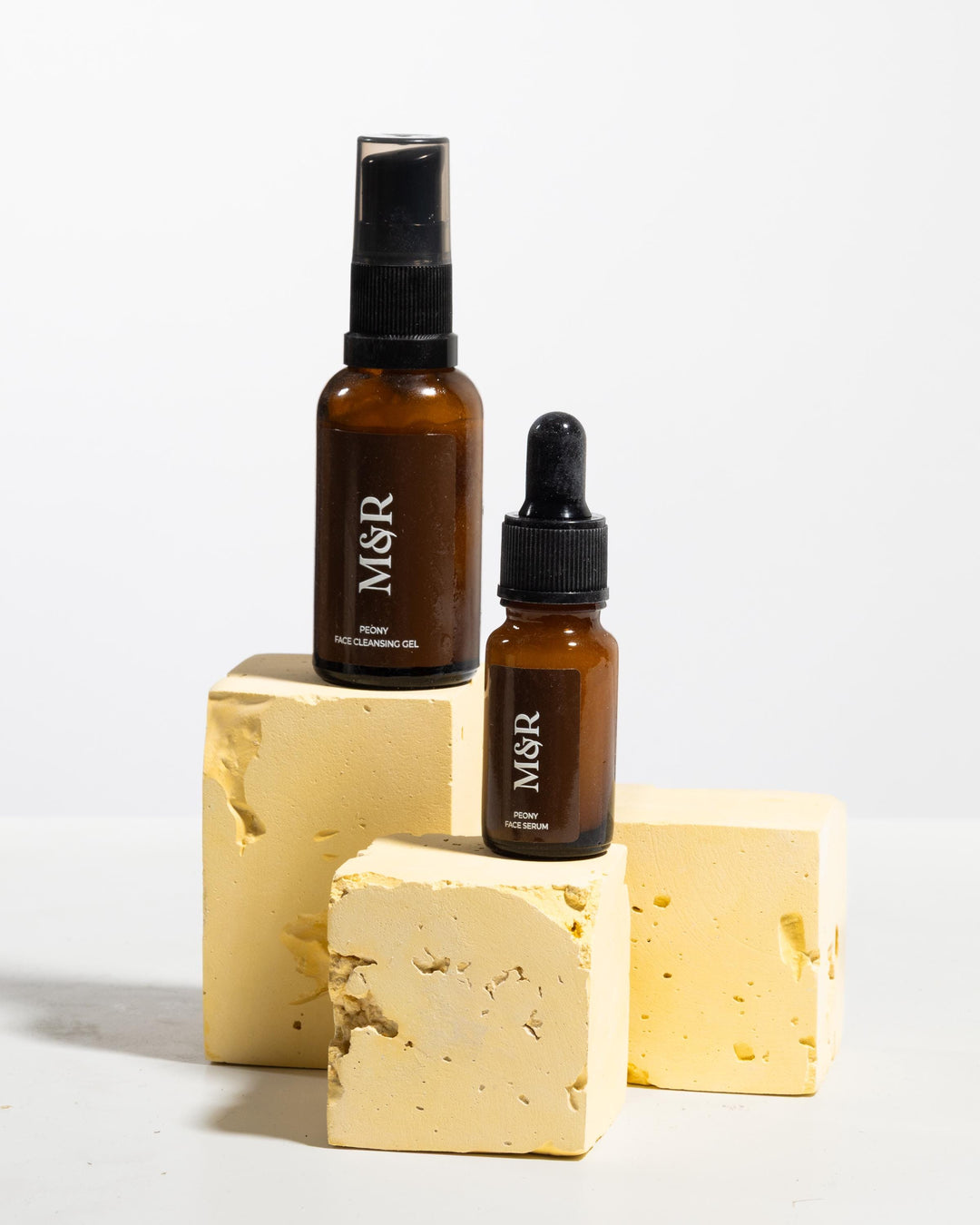Skincare bottles styled on pale yellow textured display blocks