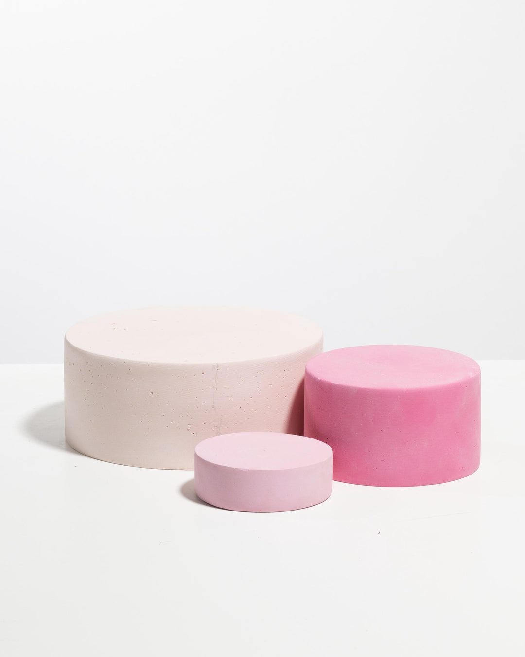 Three cylindrical soap display trays in pale blush, magenta and pastel pink